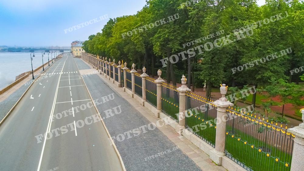 На фотографии запечатлён вид на набережную Невы и Летний сад в Санкт-Петербурге, снятый с высоты. Ограда сада украшена золотистыми элементами, и через неё видны пышные зелёные деревья. Это тихое и спокойное место города подчёркивает контраст между строгими линиями архитектуры и природной зеленью парка.